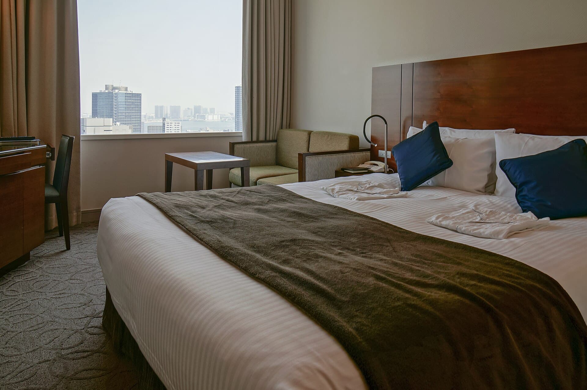 A hotel double bedroom with two beds, a window and a tidy desk