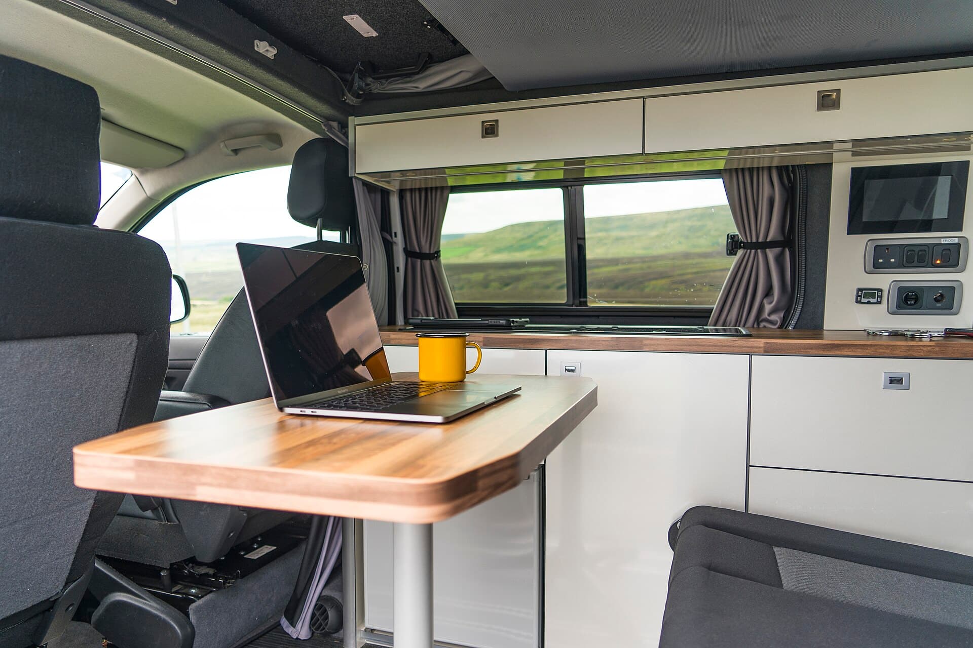 A laptop and a cup of coffee on a table in a campervan, with hills outside